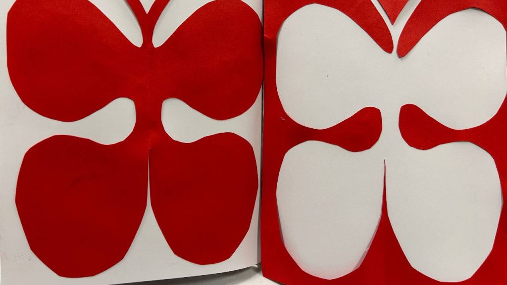 A red and white paper cutout shows symmetrical abstract shapes