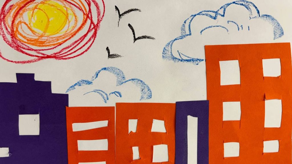 A colorful cityscape collage with orange and purple paper buildings, a crayon sun and clouds in the sky, and black birds flying.